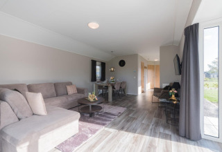 Helles, modernes Wohnzimmer einer Velthorst-Lodge in De Rijp, Niederlande, mit Sofa, Esstisch und großen Fenstern.