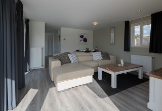 Lichte, moderne woonkamer in de Velthorst-lodge bij De Rijp, Nederland met bank, salontafel en ramen.