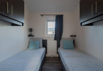 Moderne slaapkamer met twee enkele bedden, blauwe kussens en raam in een lodge te De Rijp, Nederland.