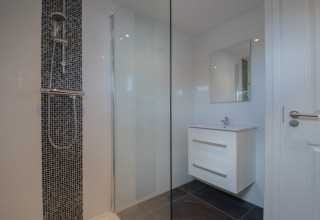 Baño moderno con baldosas en blanco y negro, ducha de vidrio y tocador blanco en Velthorst Lodge, De Rijp, Países Bajos.