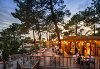 Udendørs spiseområde ved Huttopia Arcachon feriepark i Nouvelle-Aquitaine, Frankrig, omgivet af fyrretræer.