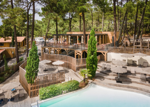 Cabañas de madera y piscina rodeadas de pinos en Huttopia Arcachon, parque vacacional en Nouvelle-Aquitaine, Francia.