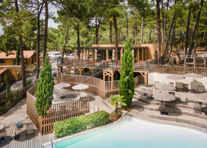 Wooden cabins and pool surrounded by pine trees at Huttopia Arcachon holiday park in Nouvelle-Aquitaine, France.