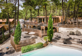 Chalets en bois et piscine entourés de pins à Huttopia Arcachon, parc de vacances en Nouvelle-Aquitaine, France.