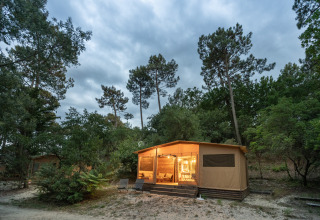 Verlichte blokhut in het bos bij Huttopia Arcachon, een vakantiepark in Nouvelle-Aquitaine, Frankrijk.
