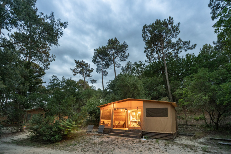 Cabane éclairée entourée de forêt au Huttopia Arcachon, un parc de vacances en Nouvelle-Aquitaine, France.