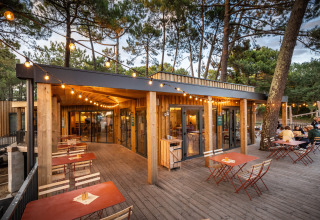 Udendørs spiseområde med træterrasse og hyggelige lyskæder på Huttopia Arcachon, Nouvelle-Aquitaine, Frankrig.