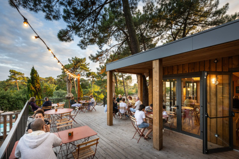 Udendørs terrasse på Huttopia Arcachon feriepark med gæster, træer og guirlandelys i Nouvelle-Aquitaine.