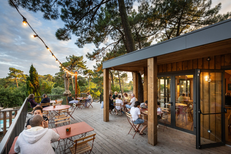 Outdoor terrace at Huttopia Arcachon holiday park with guests, trees, and string lights in Nouvelle-Aquitaine.