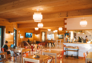 Binnenzicht van het gezellige café bij Huttopia Arcachon, Frankrijk, met houten tafels en warme sfeer.