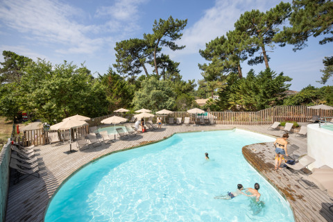 Piscina al aire libre con terraza de madera y tumbonas en Huttopia Arcachon, Nouvelle-Aquitaine, Francia.