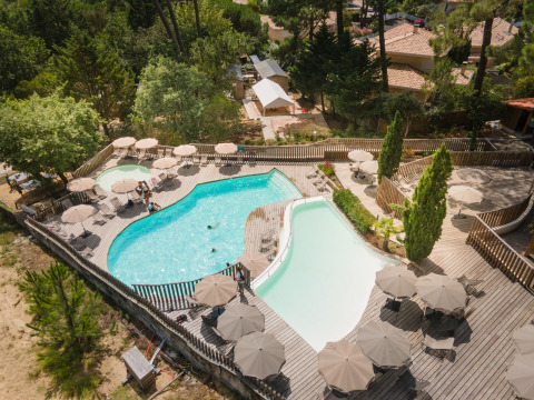 Vista aérea del área de piscina con terraza de madera y sombrillas en Huttopia Arcachon, parque vacacional en Nueva Aquitania, Francia.
