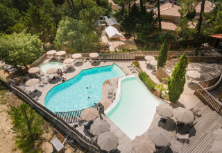 Luftaufnahme eines Pools mit Holzterrasse und Sonnenschirmen im Huttopia Arcachon Ferienpark in Nouvelle-Aquitaine, Frankreich.