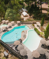 Vista aérea del área de piscina con terraza de madera y sombrillas en Huttopia Arcachon, parque vacacional en Nueva Aquitania, Francia.