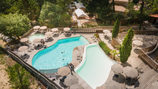 Vista aérea del área de piscina con terraza de madera y sombrillas en Huttopia Arcachon, parque vacacional en Nueva Aquitania, Francia.