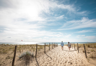 Twee personen wandelen op een zanderig pad richting zee in Huttopia Arcachon, Nouvelle-Aquitaine, Frankrijk.