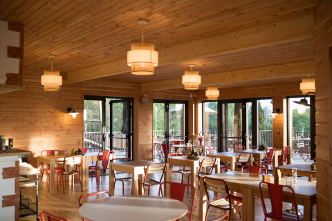 Salle à manger chaleureuse avec boiseries et grandes fenêtres à Huttopia Arcachon, Nouvelle-Aquitaine, France.