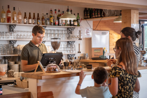 Un barista atiende a una familia en la recepción de Huttopia Arcachon en Nouvelle-Aquitaine, Francia.