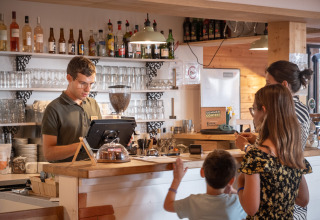 Un barista atiende a una familia en la recepción de Huttopia Arcachon en Nouvelle-Aquitaine, Francia.
