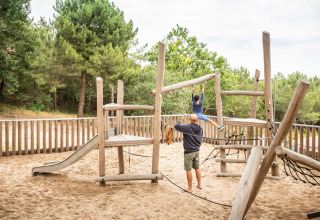 Speeltuin in het zand bij Huttopia Arcachon, Frankrijk, met houten speeltoestellen en kinderen.