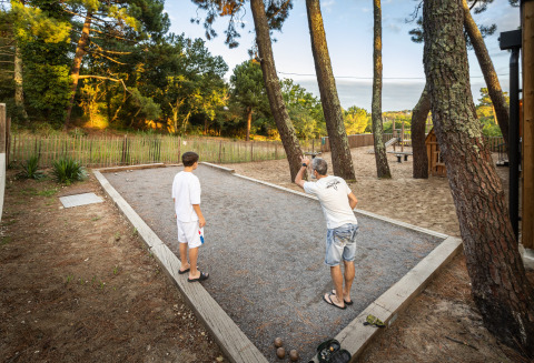Deux personnes jouent à la pétanque sur un terrain de gravier entouré d’arbres à Huttopia Arcachon, France.