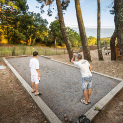 Dos personas juegan a la petanca en una pista de grava rodeada de árboles en Huttopia Arcachon, Francia.