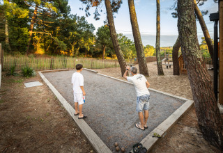 Due persone giocano a pétanque su un campo di ghiaia tra gli alberi a Huttopia Arcachon, Francia.