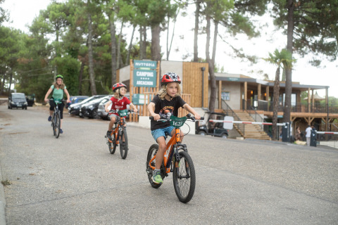 Bambini e un adulto in bicicletta davanti al villaggio Huttopia Arcachon in Nouvelle-Aquitaine, Francia, tra gli alberi.