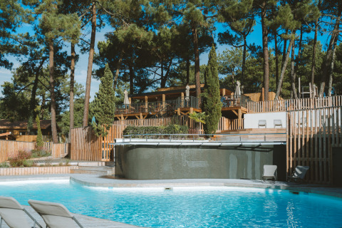Piscina al aire libre con tumbonas, rodeada de pinos en Huttopia Arcachon, en Nouvelle-Aquitaine, Francia.