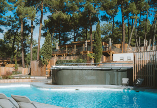 Outdoor swimming pool with lounge chairs, surrounded by pine trees at Huttopia Arcachon, Nouvelle-Aquitaine, France.