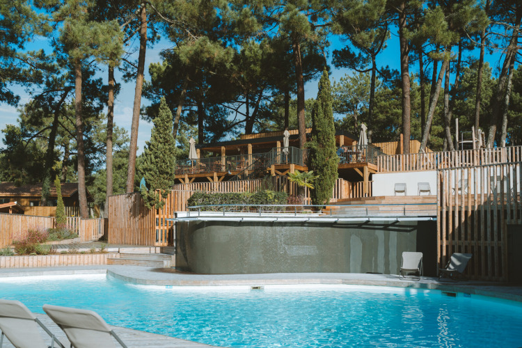 Outdoor swimming pool with lounge chairs, surrounded by pine trees at Huttopia Arcachon, Nouvelle-Aquitaine, France.
