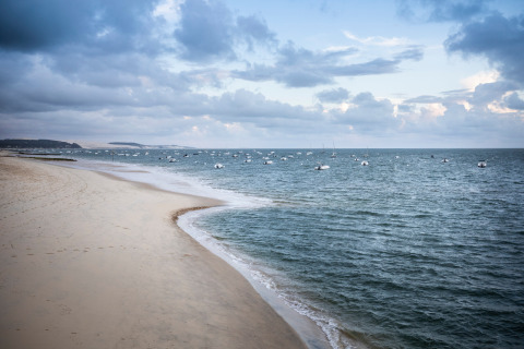 Strand og hav med både ved Arcachon, Nouvelle-Aquitaine, Frankrig, under en overskyet himmel.