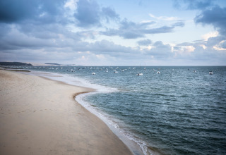 Plage de sable et bateaux près d’Arcachon, Nouvelle-Aquitaine, France, sous un ciel nuageux.