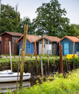 Casetas de madera de colores y un velero junto a la orilla cerca de Arcachon, rodeadas de naturaleza.
