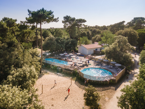 Aerial view of Huttopia Oléron les Pins holiday park in France, showing pools, volleyball, and pine trees.