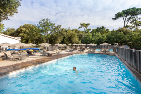 Piscina al aire libre en Huttopia Oléron les Pins, rodeada de tumbonas y sombrillas en un entorno natural.