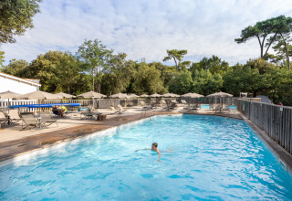 Outdoor swimming pool at Huttopia Oléron les Pins holiday park, surrounded by sun loungers and umbrellas.