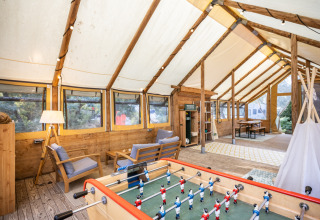 Indbydende interiør af et telt på Huttopia Oléron les Pins, med sofaer, bordfodbold og store vinduer.