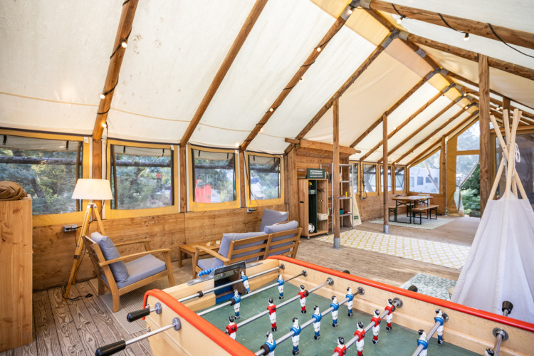 Inviting tent interior at Huttopia Oléron les Pins with sofas, foosball table, and large scenic windows.