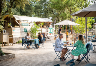 Udendørs caféområde på Huttopia Oléron les Pins, folk nyder mad og drikke under parasoller i Frankrig.