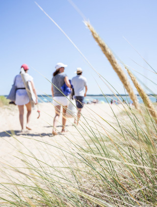 Tres personas caminan por una playa de arena con dunas cerca de Saint Trojan les Bains, Nouvelle-Aquitaine, Francia.