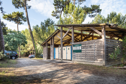 Edificio sanitario al aire libre entre pinos en Huttopia Oléron les Pins, parque vacacional en Nouvelle-Aquitaine, Francia.