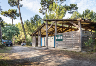 Udendørs sanitetsbygning omgivet af fyrretræer i Huttopia Oléron les Pins, en feriepark i Nouvelle-Aquitaine.