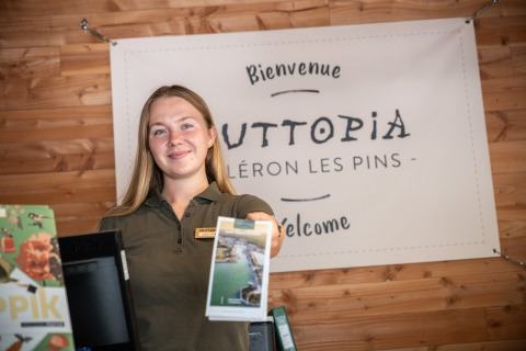 Una recepcionista sonriente da la bienvenida a los huéspedes en la entrada del parque vacacional Huttopia Oléron les Pins en Francia.