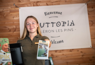 Una recepcionista sonriente da la bienvenida a los huéspedes en la entrada del parque vacacional Huttopia Oléron les Pins en Francia.