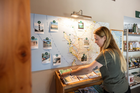 Una mujer observa mapas y folletos en la zona de información de Huttopia Oléron les Pins, Nouvelle-Aquitaine.