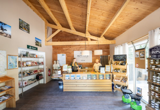 Butiksområde med træloft og varer på hylder i receptionen på Huttopia Oléron les Pins feriepark, Frankrig.