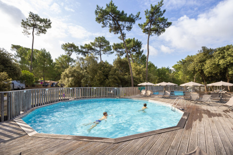 Dos niños nadan en una piscina circular rodeada de terraza de madera y árboles en Huttopia Oléron les Pins.
