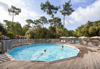 Zwei Kinder schwimmen im runden Pool mit Holzterrasse, Sonnenschirmen und Bäumen im Huttopia Oléron les Pins.