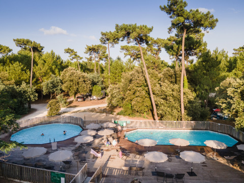 Piscina al aire libre en Huttopia Oléron les Pins, rodeada de árboles en Nouvelle-Aquitaine, Francia.
